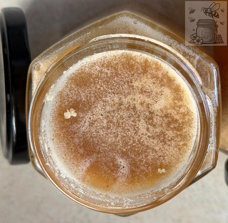 A jar of honey with a light foamy top layer