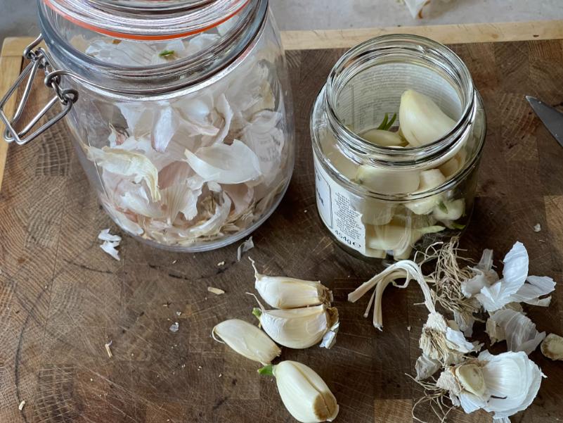 Glass jars filled with peeled garlic cloves and raw honey on a rustic wooden surface, with fresh garlic skins and cloves scattered around.